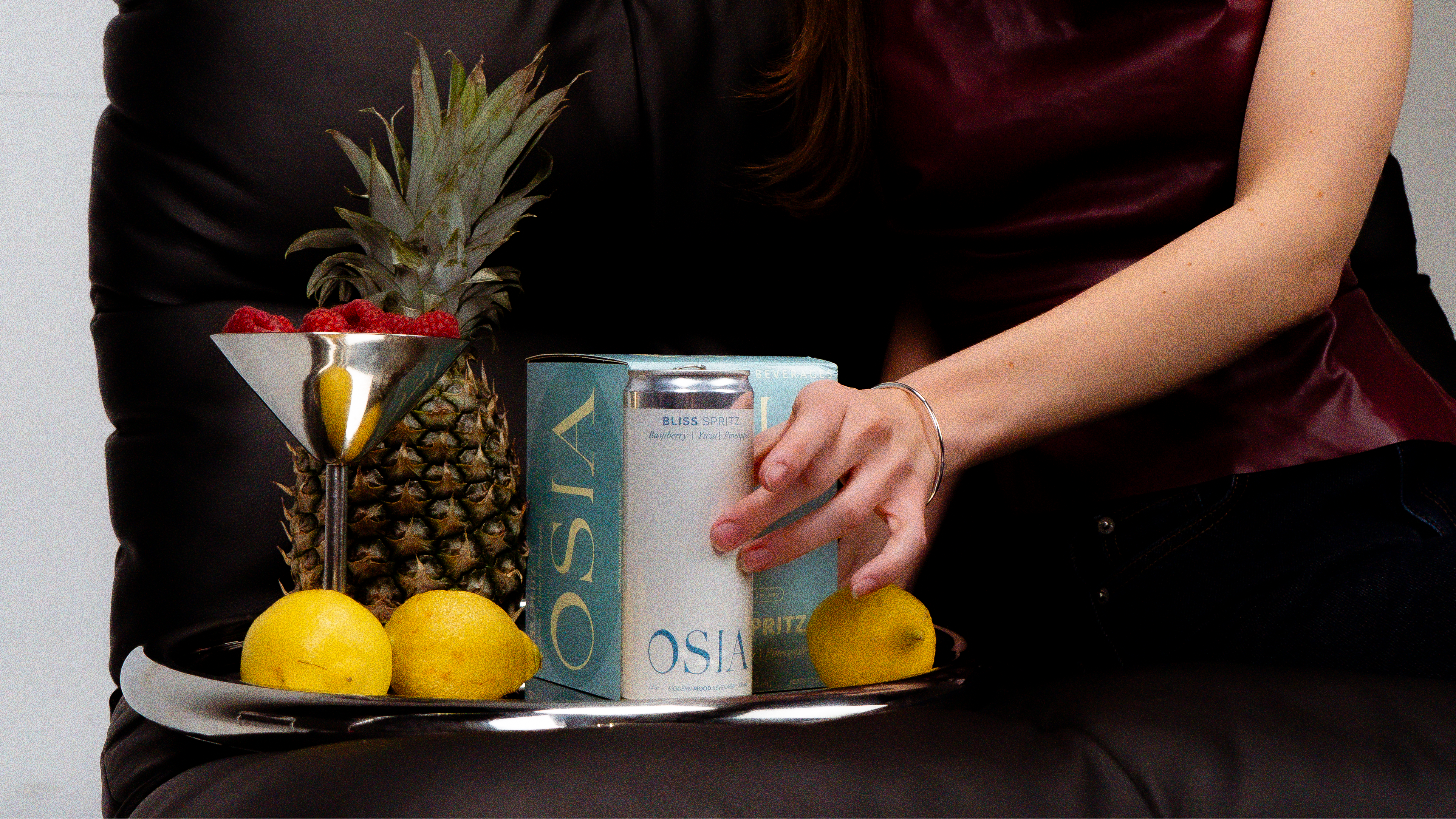 Person holding a can of OSIA next to lemons and a pineapple on a tray.