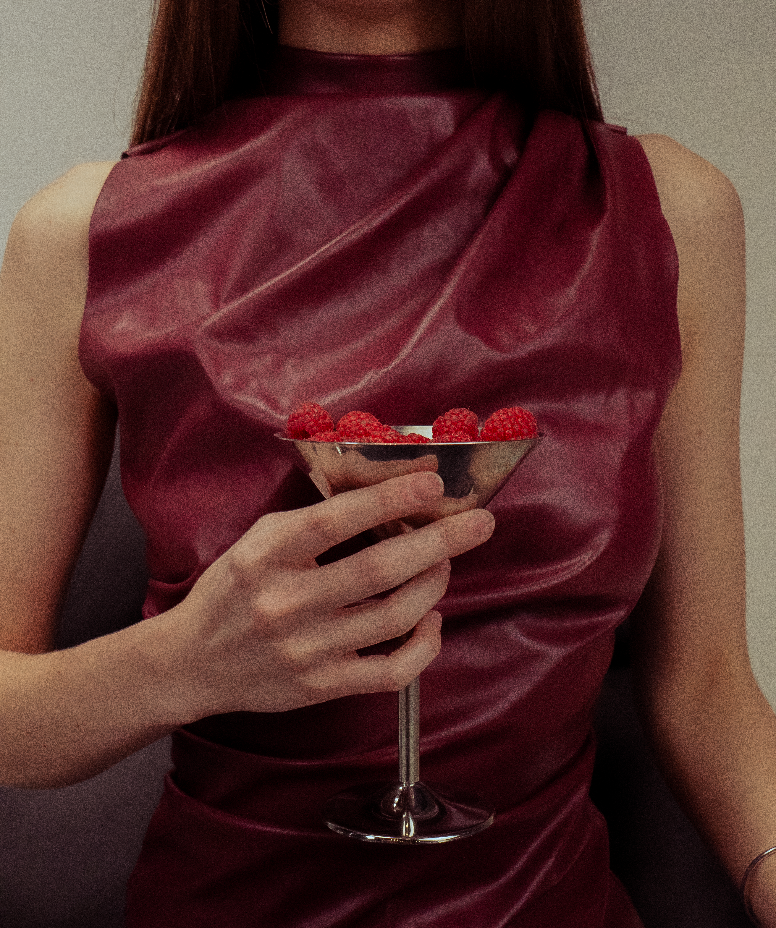 Person wearing a burgundy satin top holding a cocktail with red berries.
